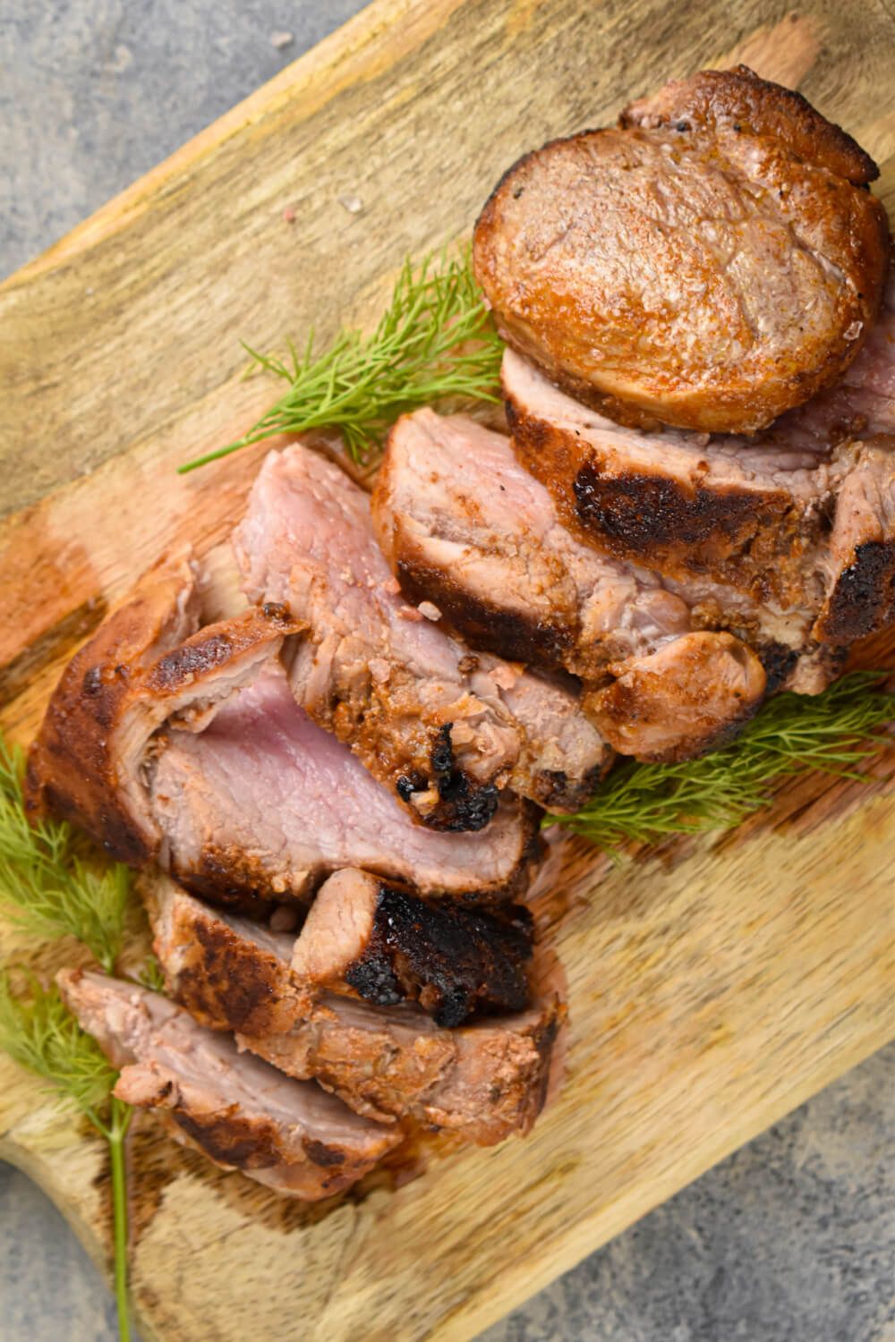 Barbecue pork tenderloin on a wooden cutting board with rosemary.