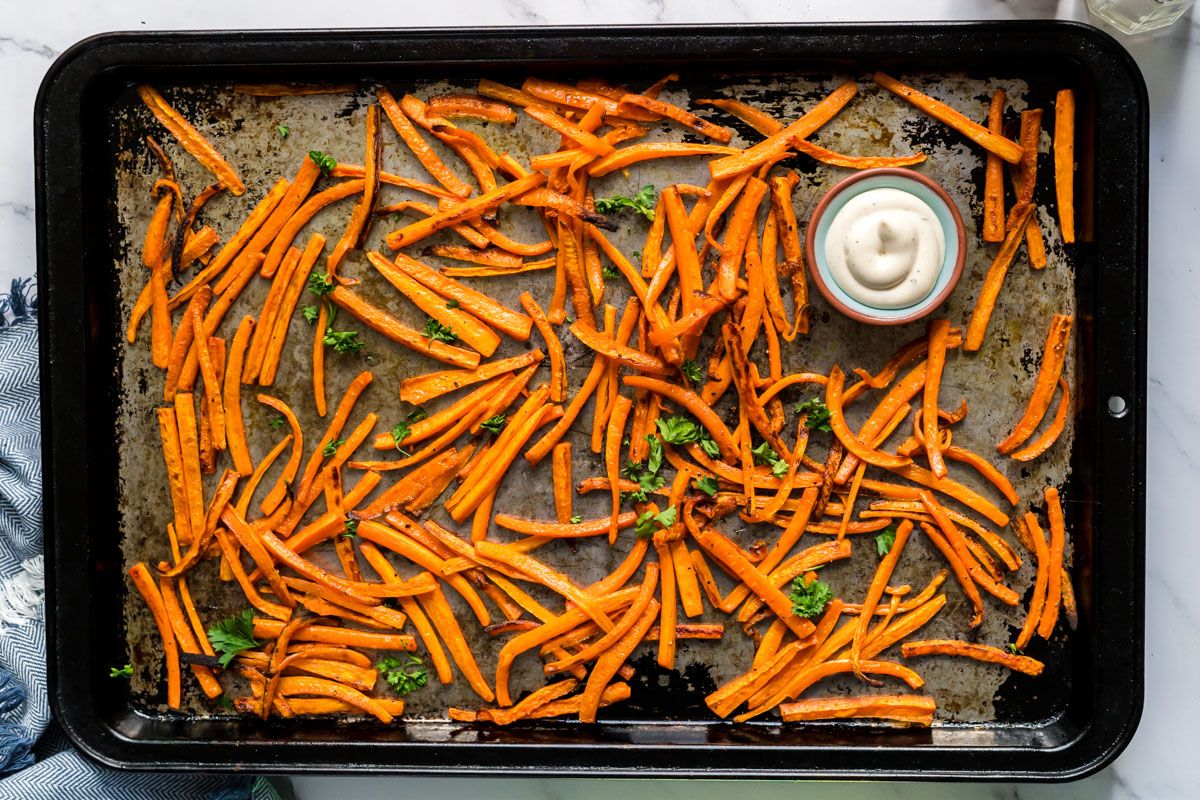 Baked carrot fries on a sheet pan with salt, pepper, fresh herbs, and ranch dipping sauce.