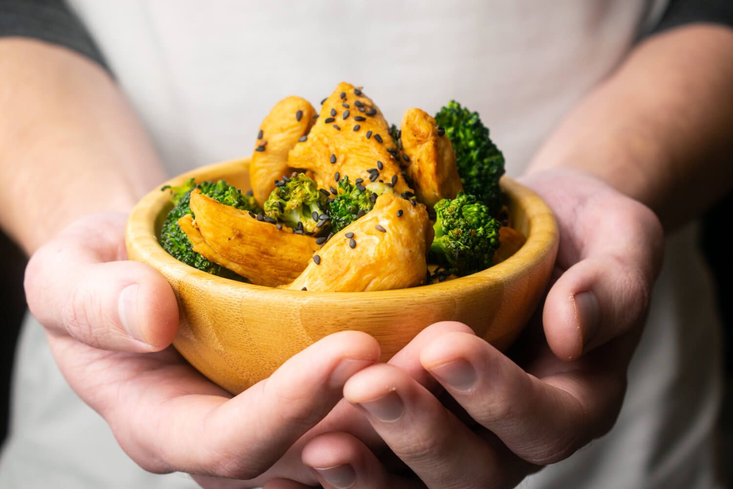 Bowl of chicken and broccoli stir fry being held with two hands.