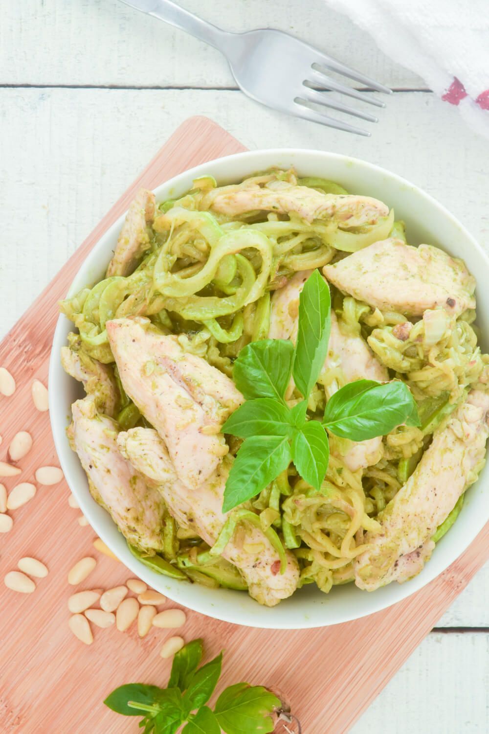 Pesto zoodles in a bowl with chicken and pine nuts.