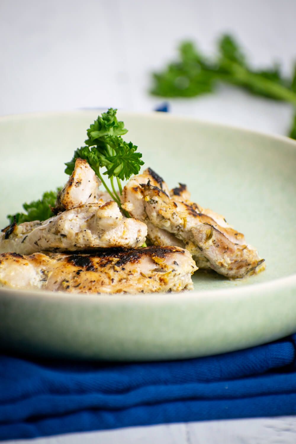 Grilled Greek chicken thighs with herbs, lemon, and garlic on a plate with parsley.