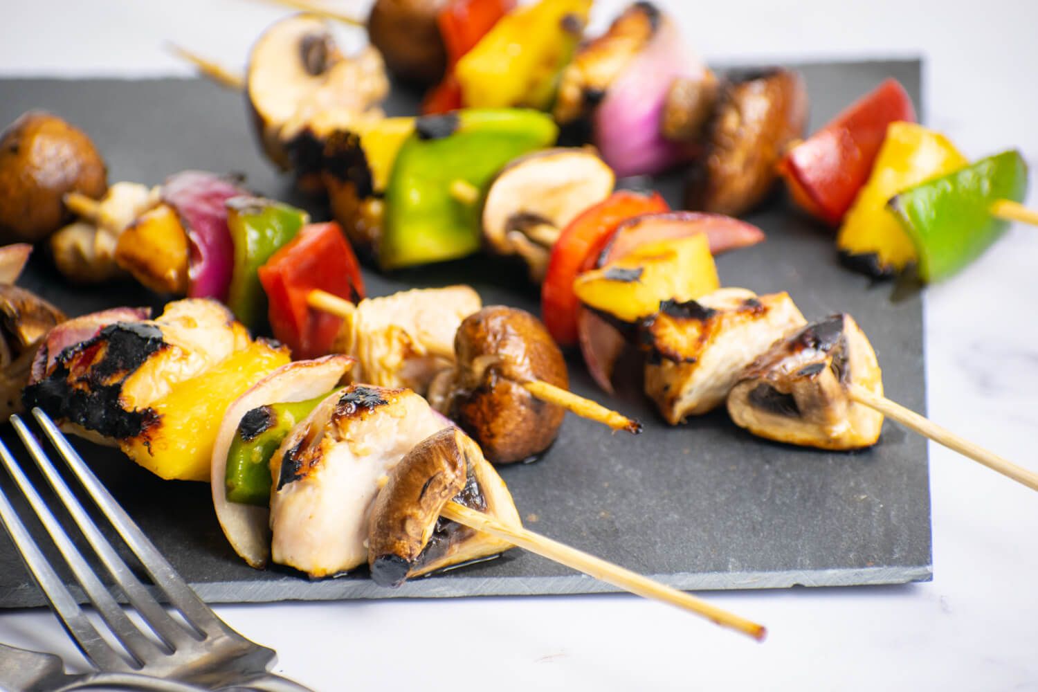 Chicken and pineapple kabobs with onions, peppers, and mushrooms on wooden skewers.