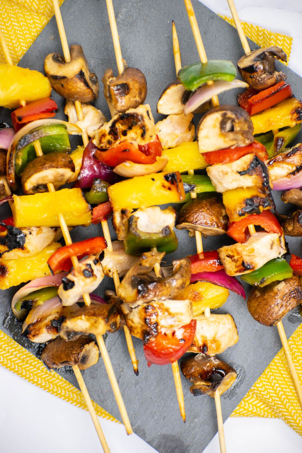 Chicken Pineapple Kabobs with peppers, mushrooms, and onions on skewers with a yellow napkin.