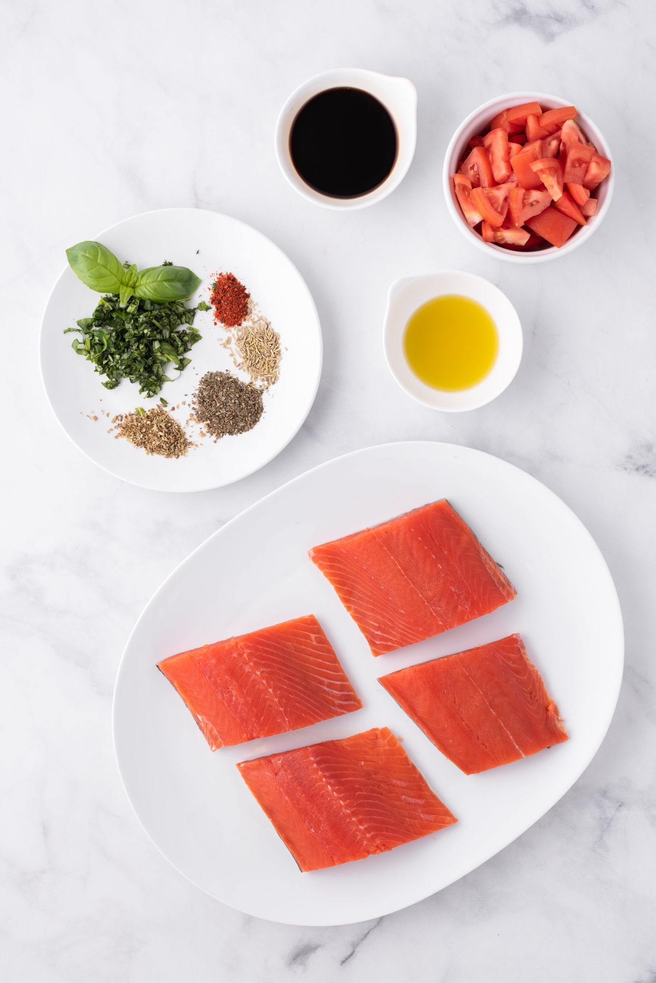 Ingredients for Italian salmon including salmon filets, tomatoes, olive oil, fresh basil, and spices.