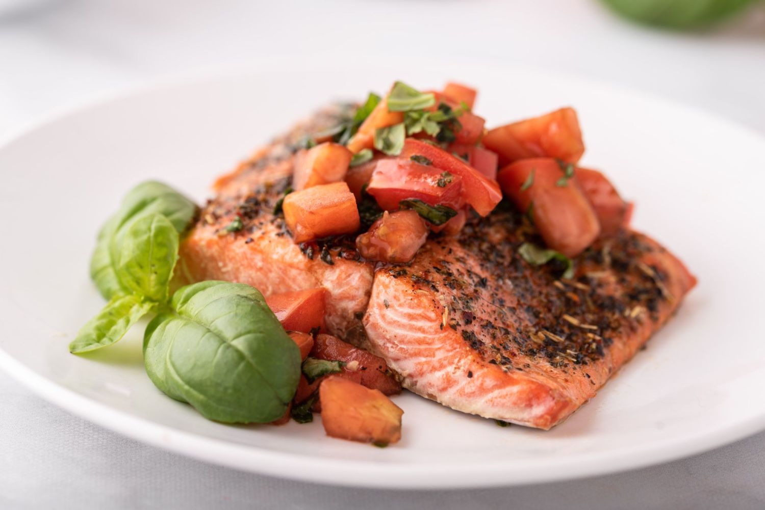 Broiled salmon with Italian seasoning and tomato salsa on top on a white plate.