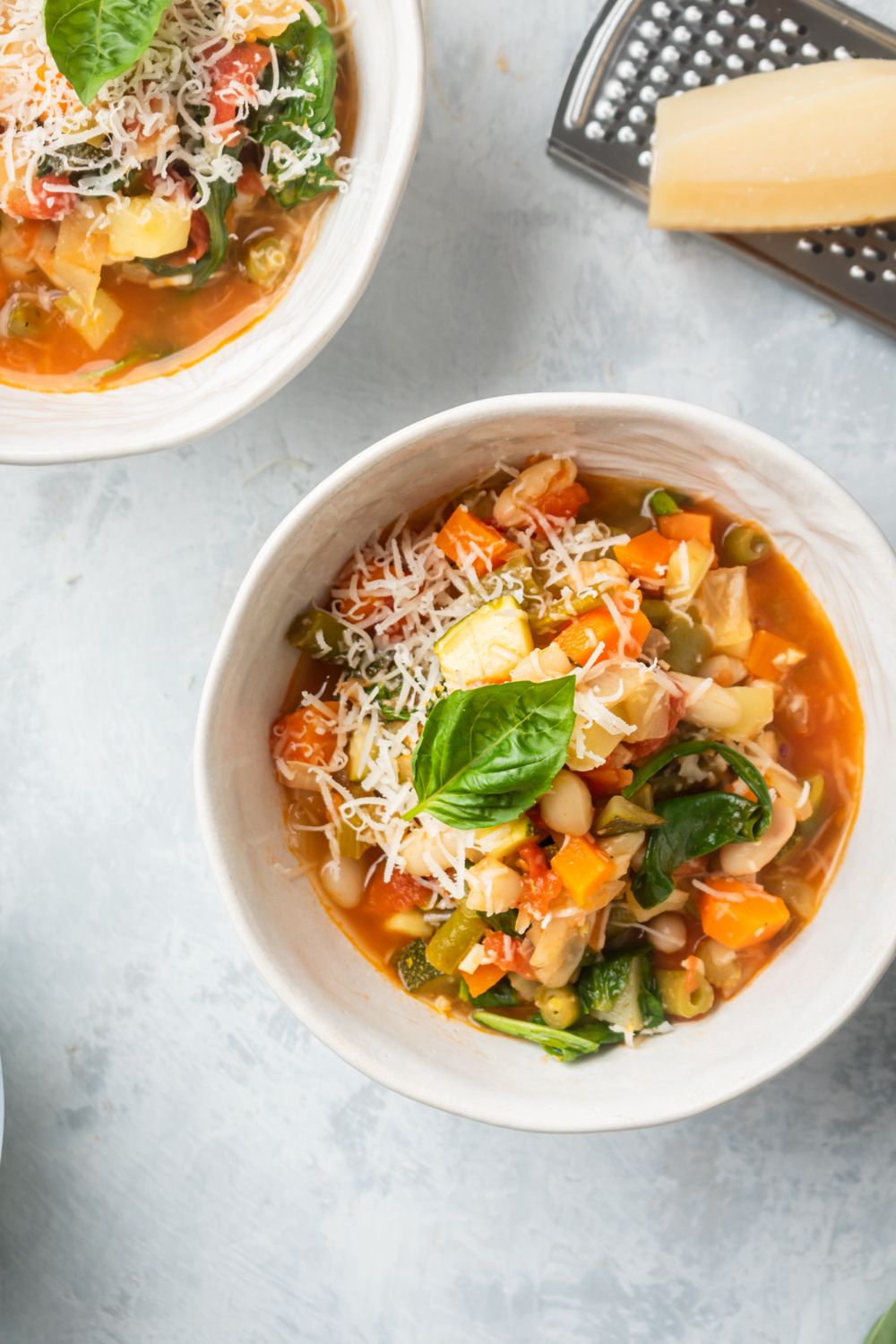 Vegetable and bean soup served basil and Parmesan cheese in white bowls.