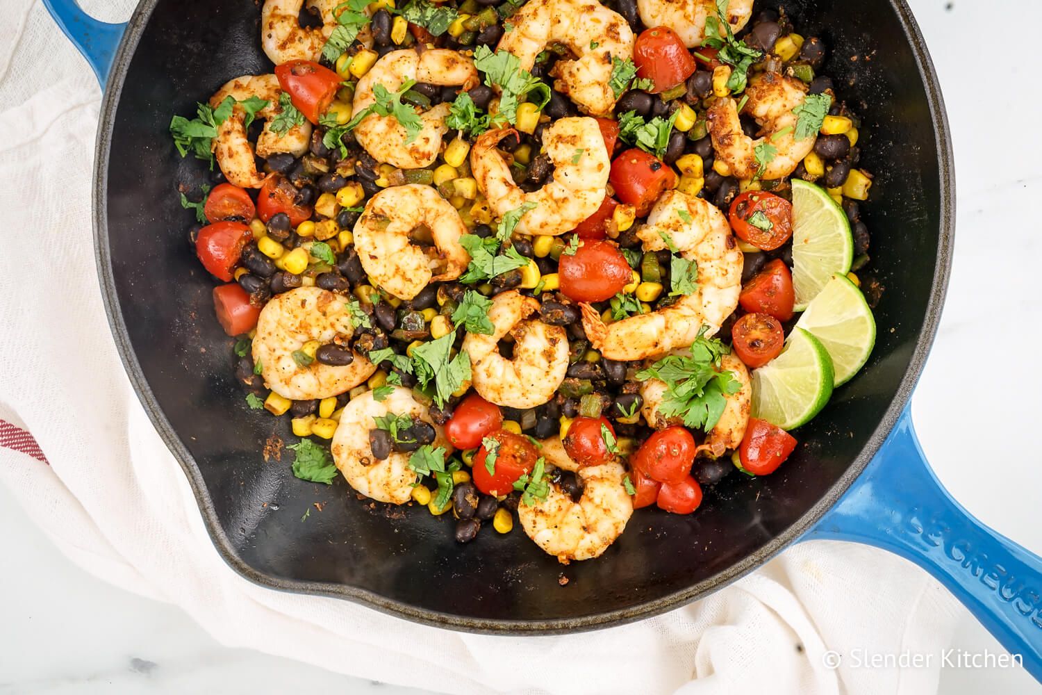 Mexican spiced shrimp in a skillet with black beans, corn, cherry tomatoes, and lime juices.