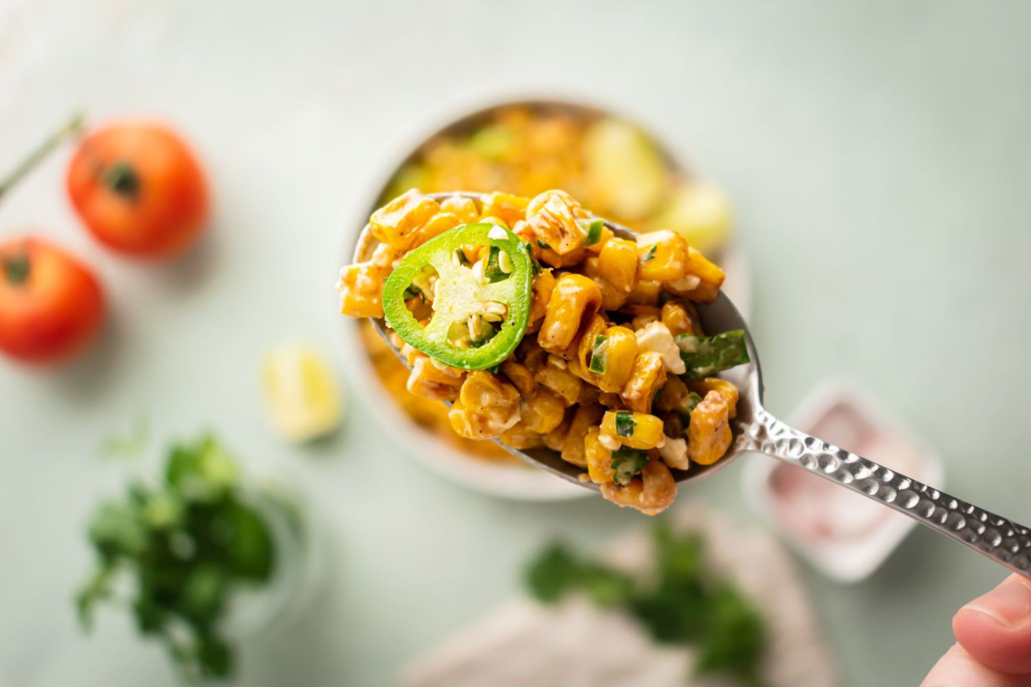 Street corn salad on a spoon with creamy corn, Cotija cheese, and a sliced fresh jaalpeno.