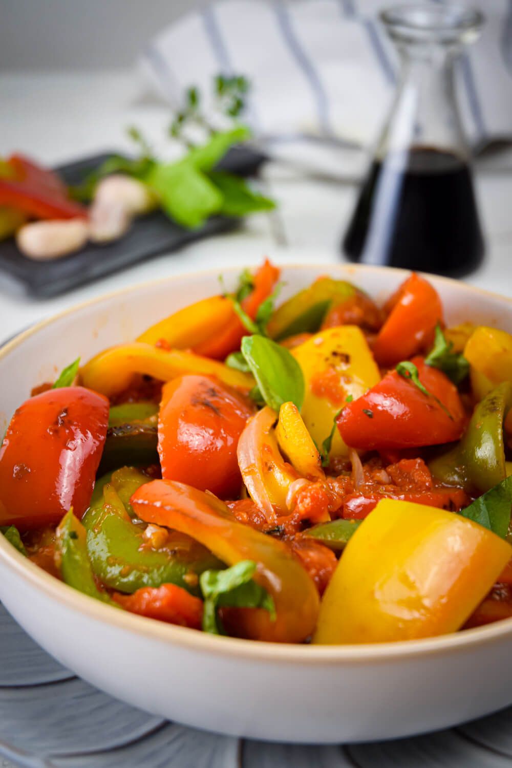 Pepperonata with green, red, and yellow bell peppers with onions, garlic, and tomatoes in a bowl.