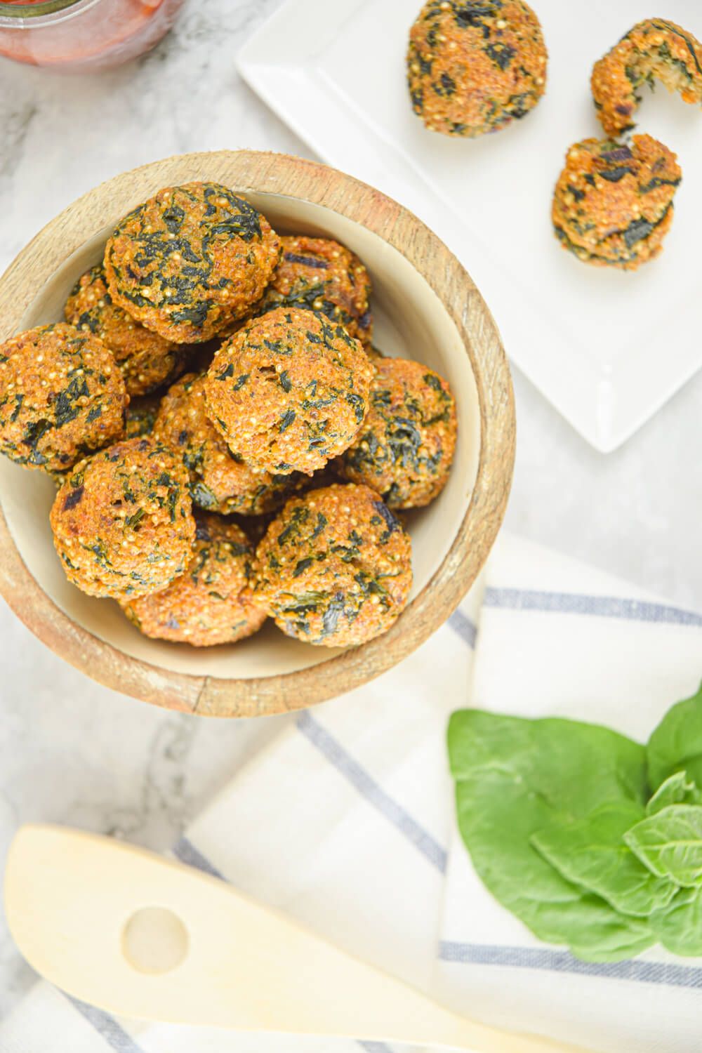 Quinoa spinach meatballs in a wooden bowl with marinara sauce on the side.