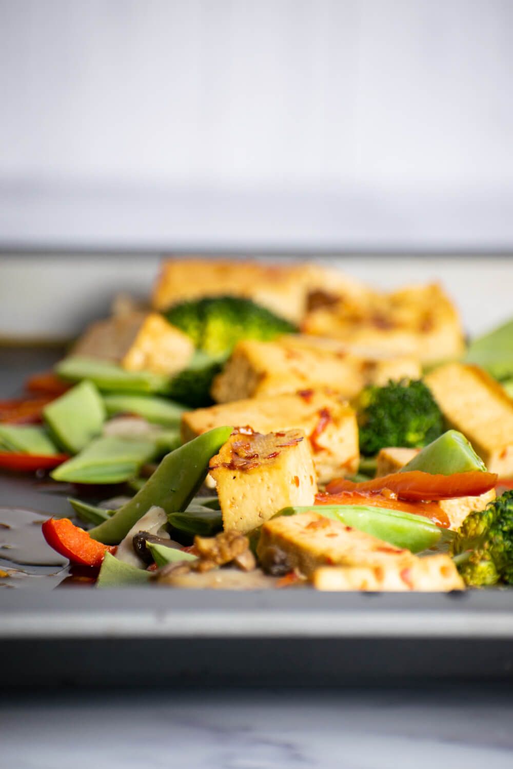 Sheet pan tofu with vegetables in asian sauce on a baking pan.