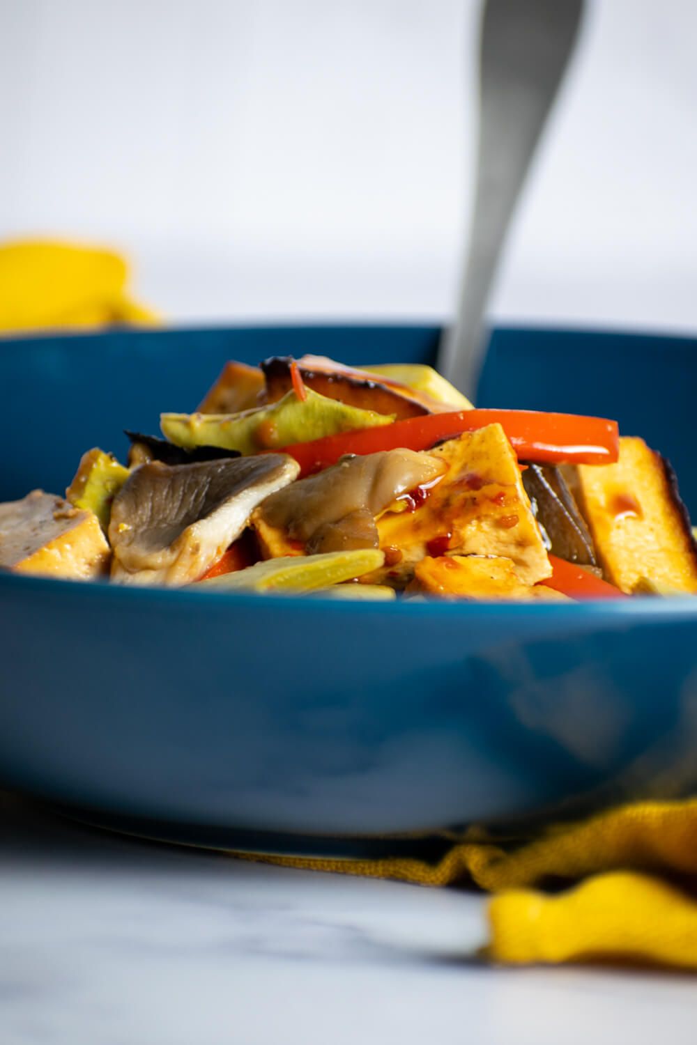 Sheet pan tofu, peas, mushrooms, and carrots in a blue bowl.