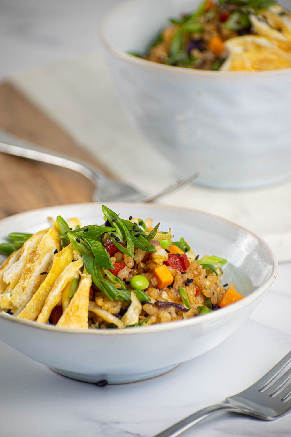 Vegetable and egg fried rice with cabbage, carrots, peas, green onions, brown rice, and eggs in a bowl with a fork.