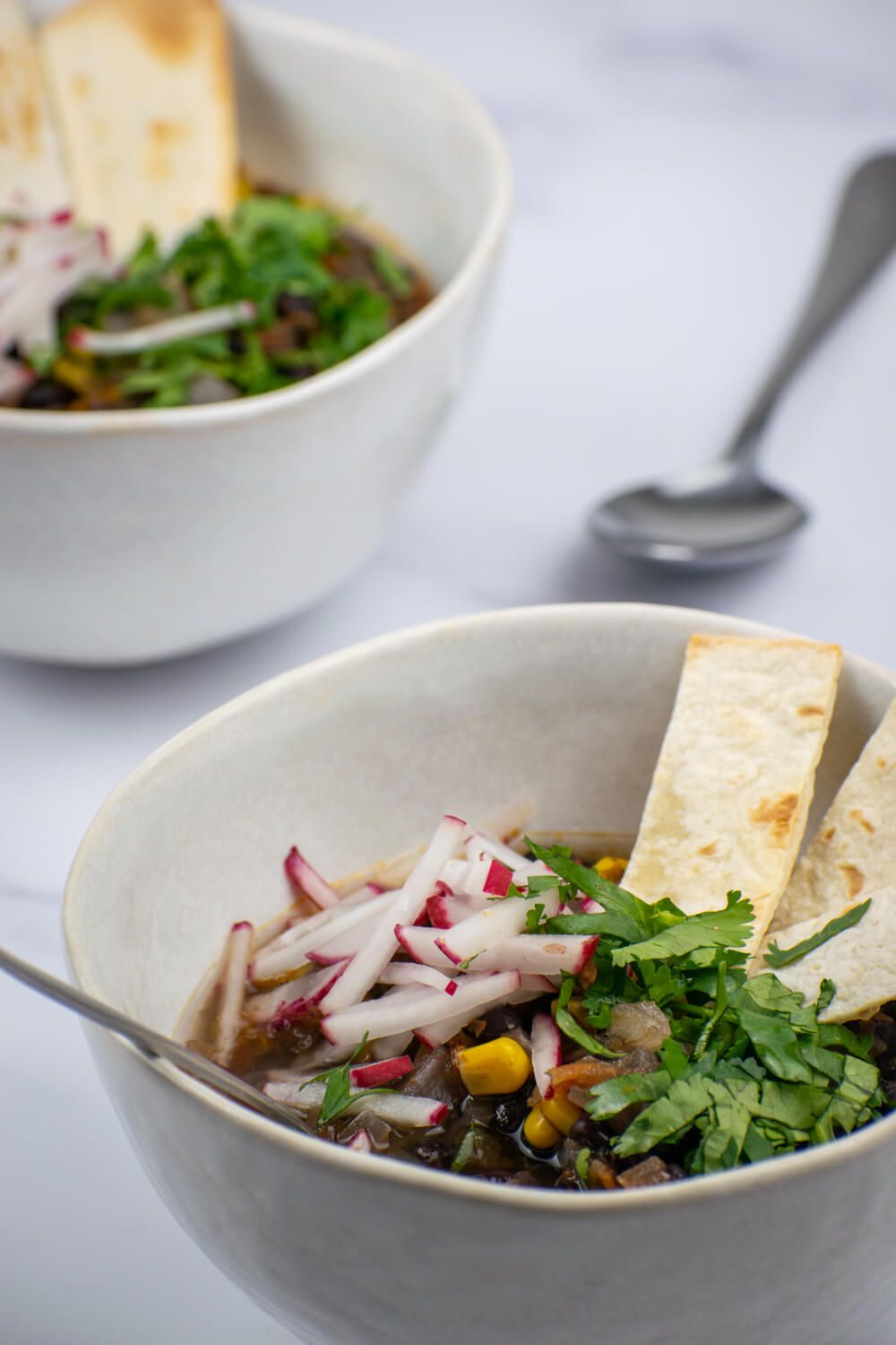 Vegetarian tortilla soup with black beans, corn, and hominy topped with cilantro and radishes.