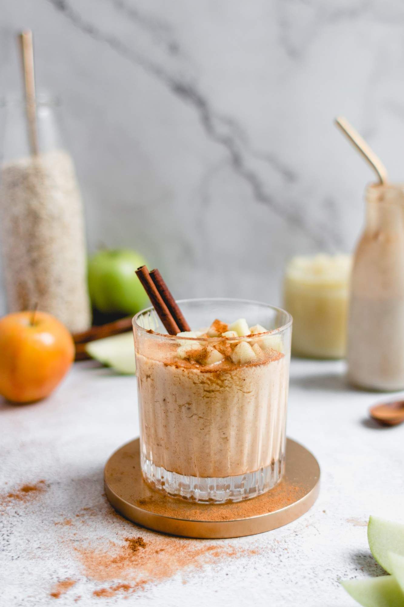 Banana and apple smoothie in a glass with a cinnamon stick, chopped apples, and bananas. 