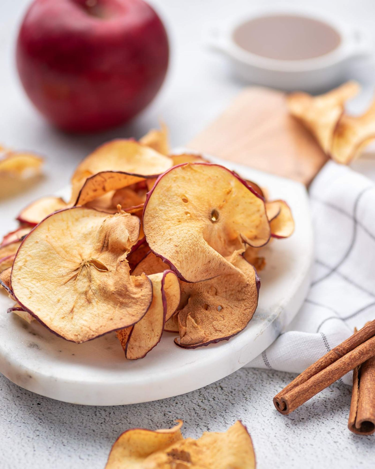 Cinnamon baked apple chips on a plate with apples and cinnamon sticks on the side.