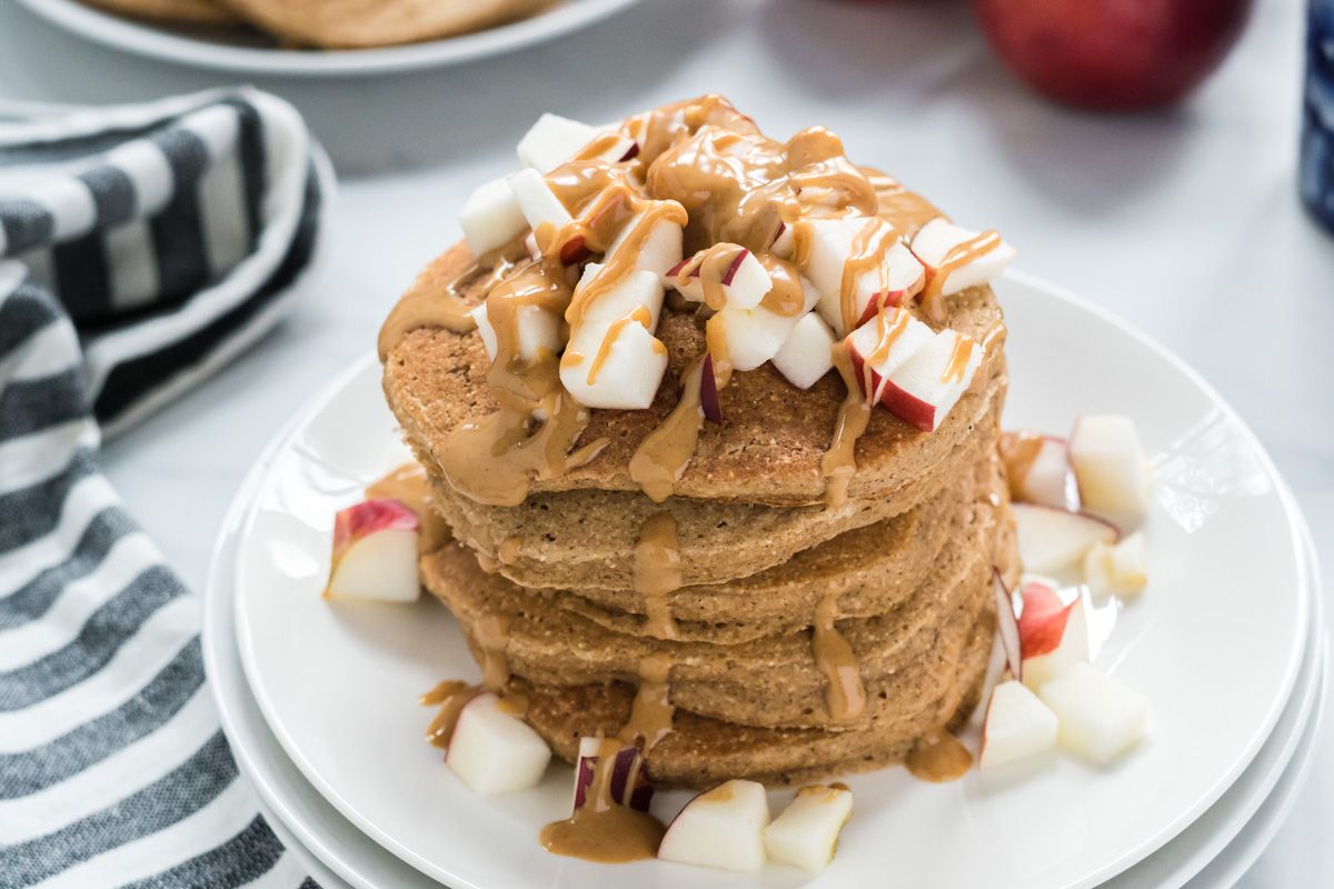 Pancakes with apple and cinnamon on a plate with peanut butter and chopped apples.