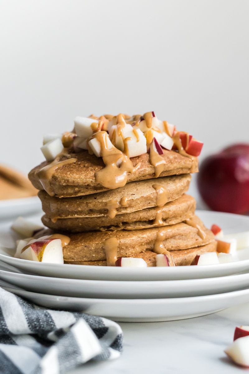 Oatmeal apple cinnamon pancakes in a stack with fresh apples and peanut butter.