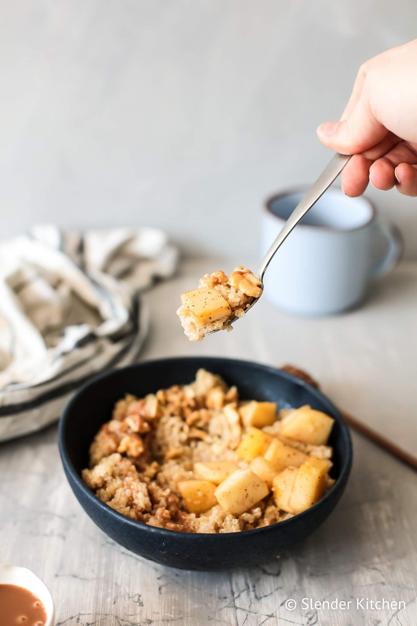 Quinoa breakfast bowls with apples, cinnamon, and caramel sauce being lifted on a spoon.