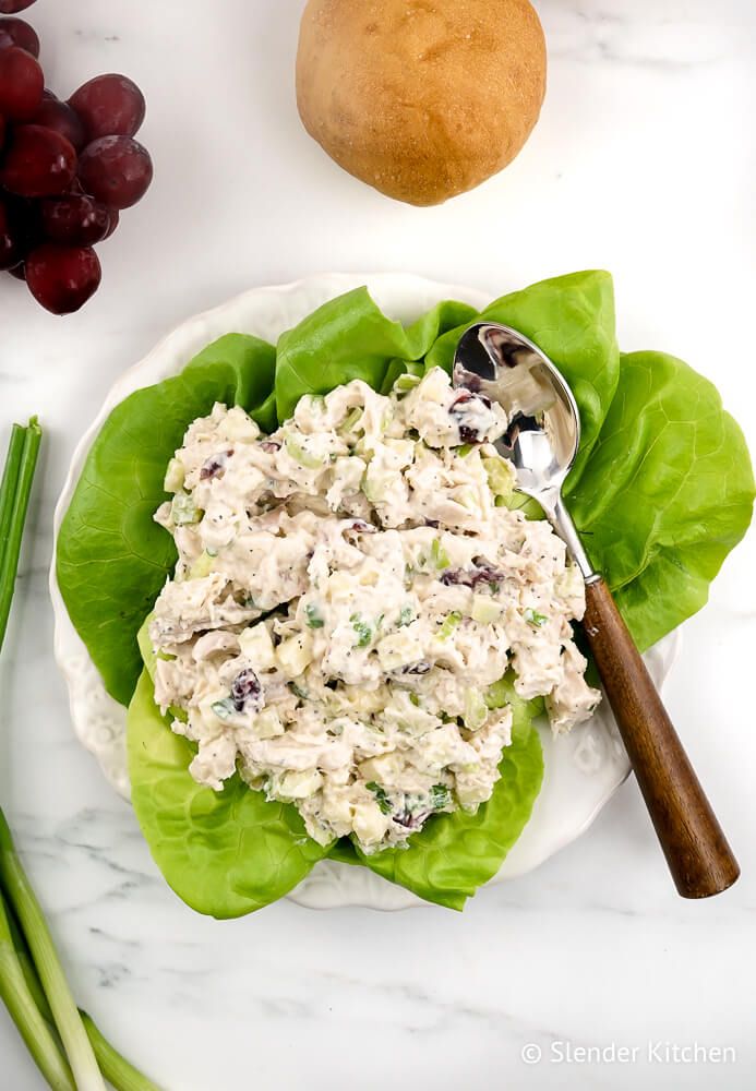 Cranberry chicken salad with apples in a bowl with grapes and bread.