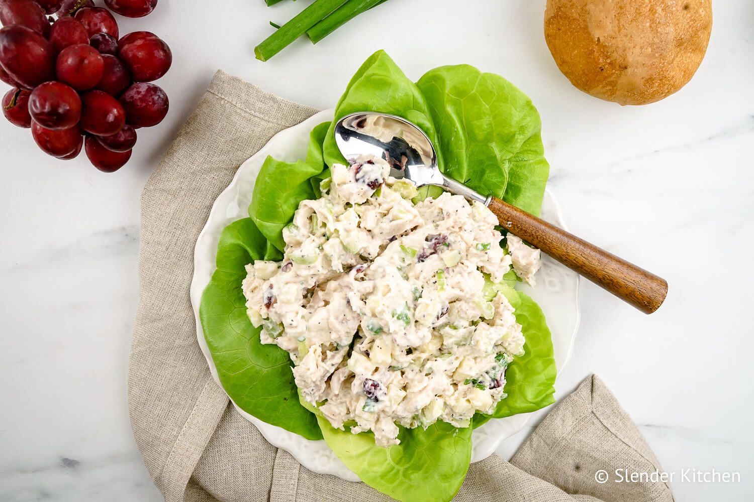 Cranberry chicken salad with a wooden spoon and red grapes.