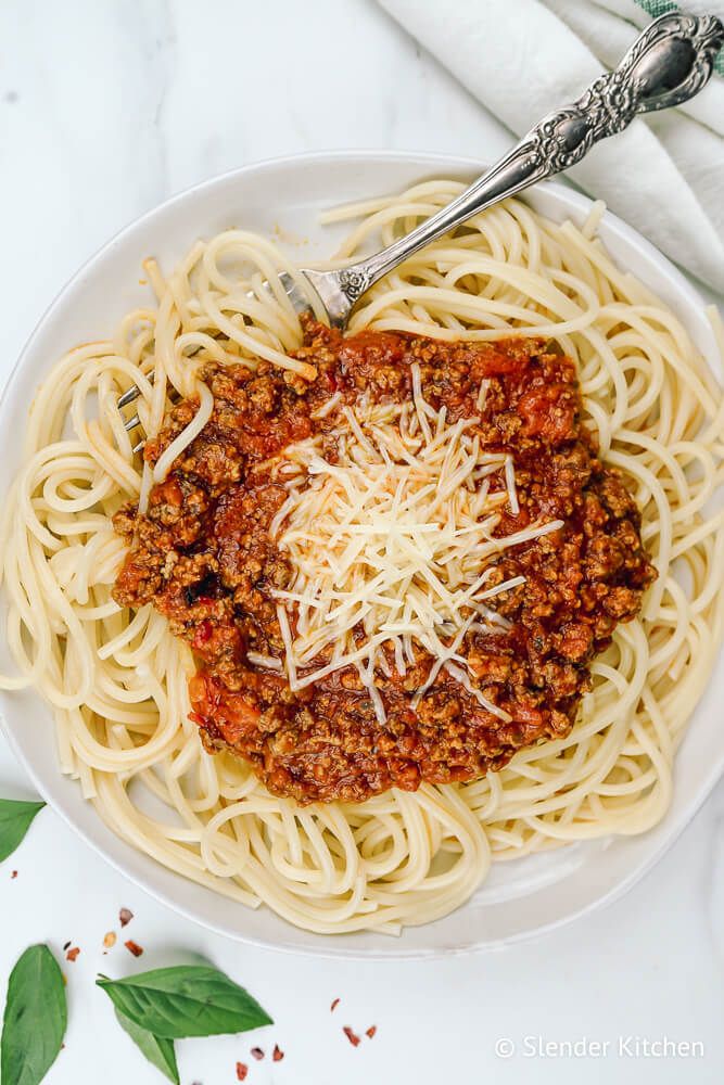 Spaghetti Arrabiata on a white plate with Parmesan cheese and basil.