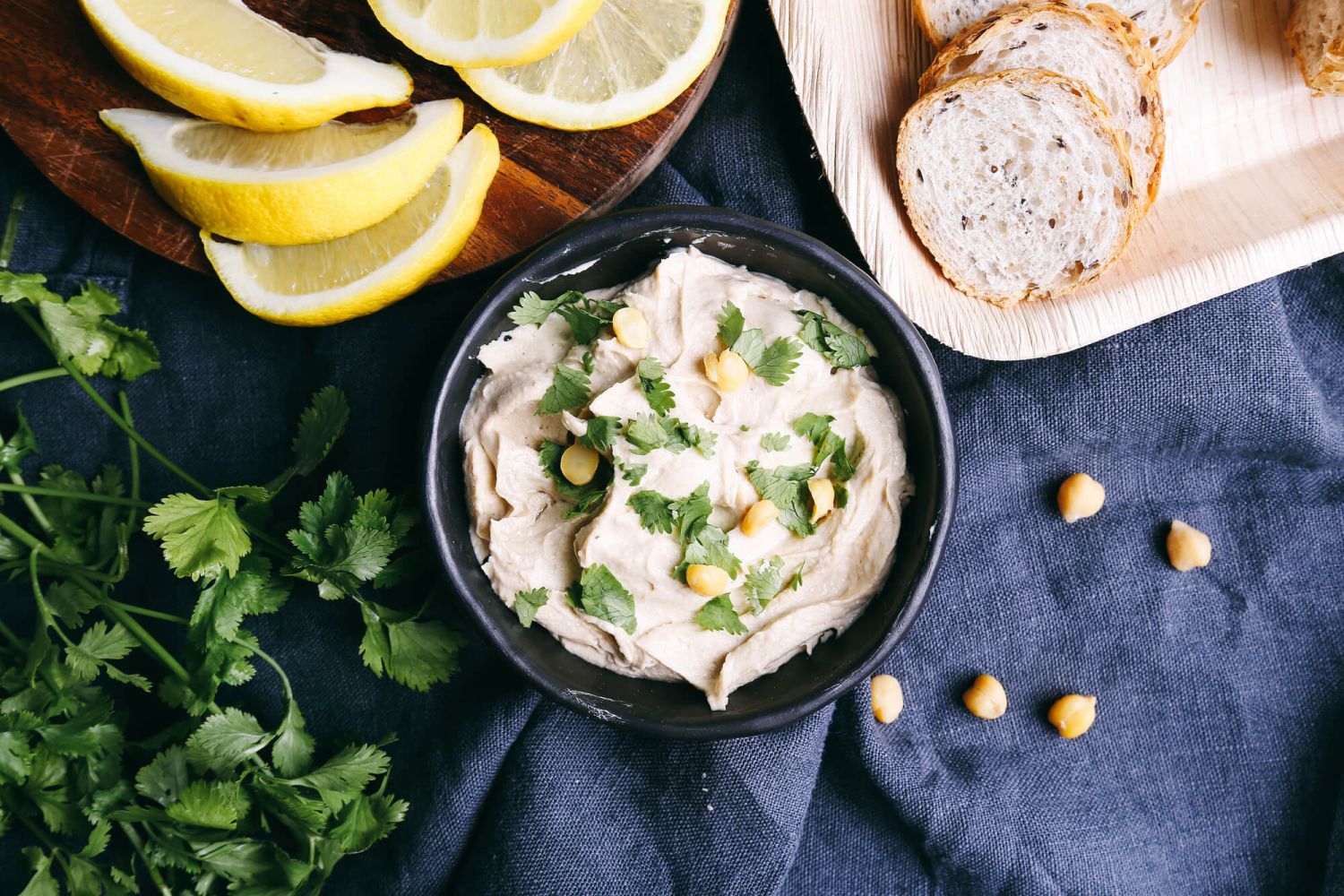 Hummus with artichokes, lemons, and herbs on a cutting board.