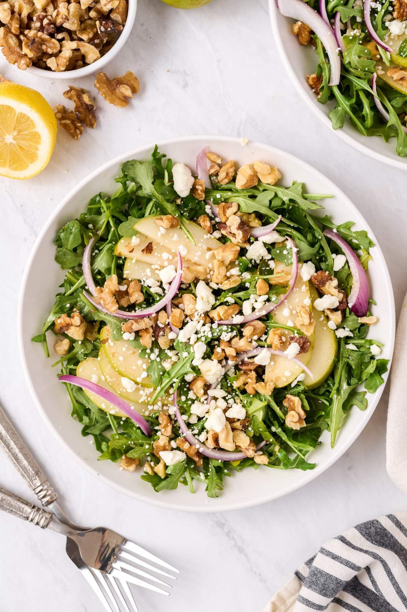 Arugula and pear salad with goat cheese, toasted walnuts, and red onions in a large bowl with vinaigrette.