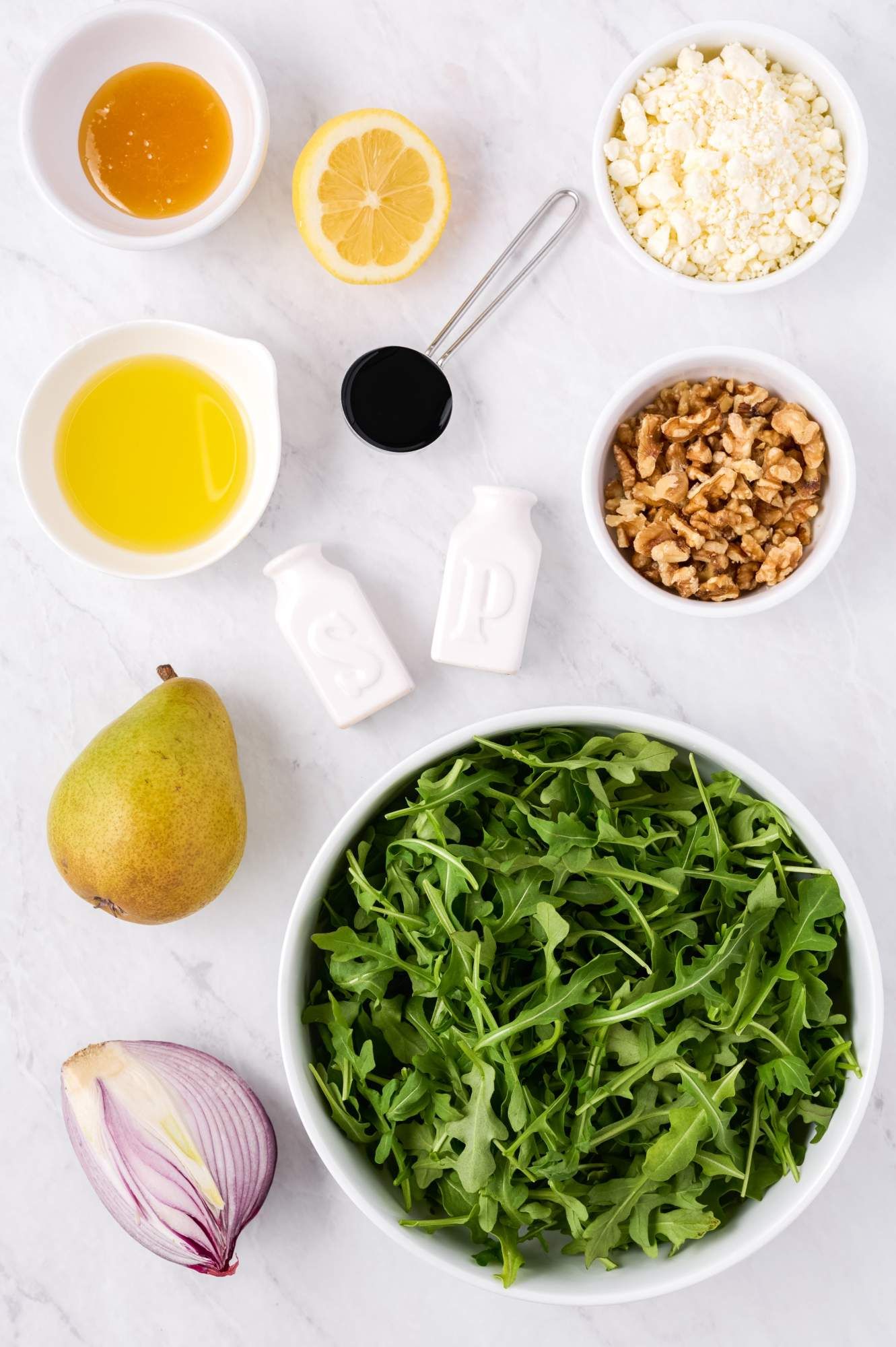 Ingredients for arugula salad including pears, walnuts, goat cheese, fresh arugula, red onion, and vinaigrette.