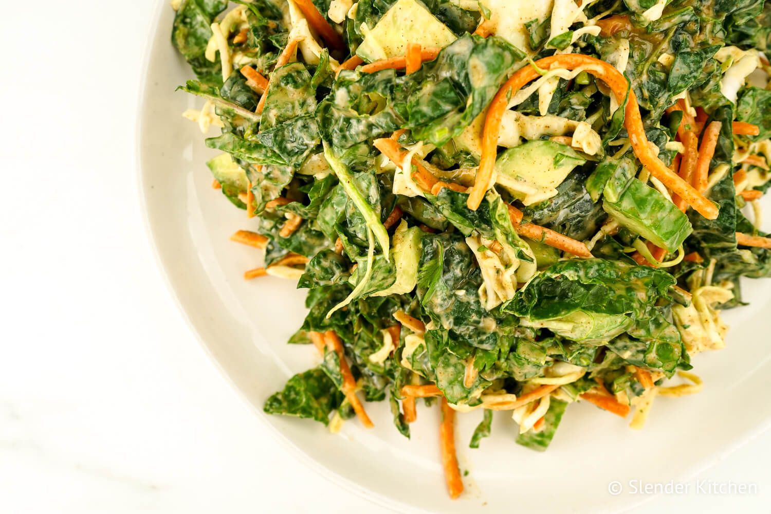 Kale slaw with apples, cucumbers, and fresh herbs on a white ceramic plate.