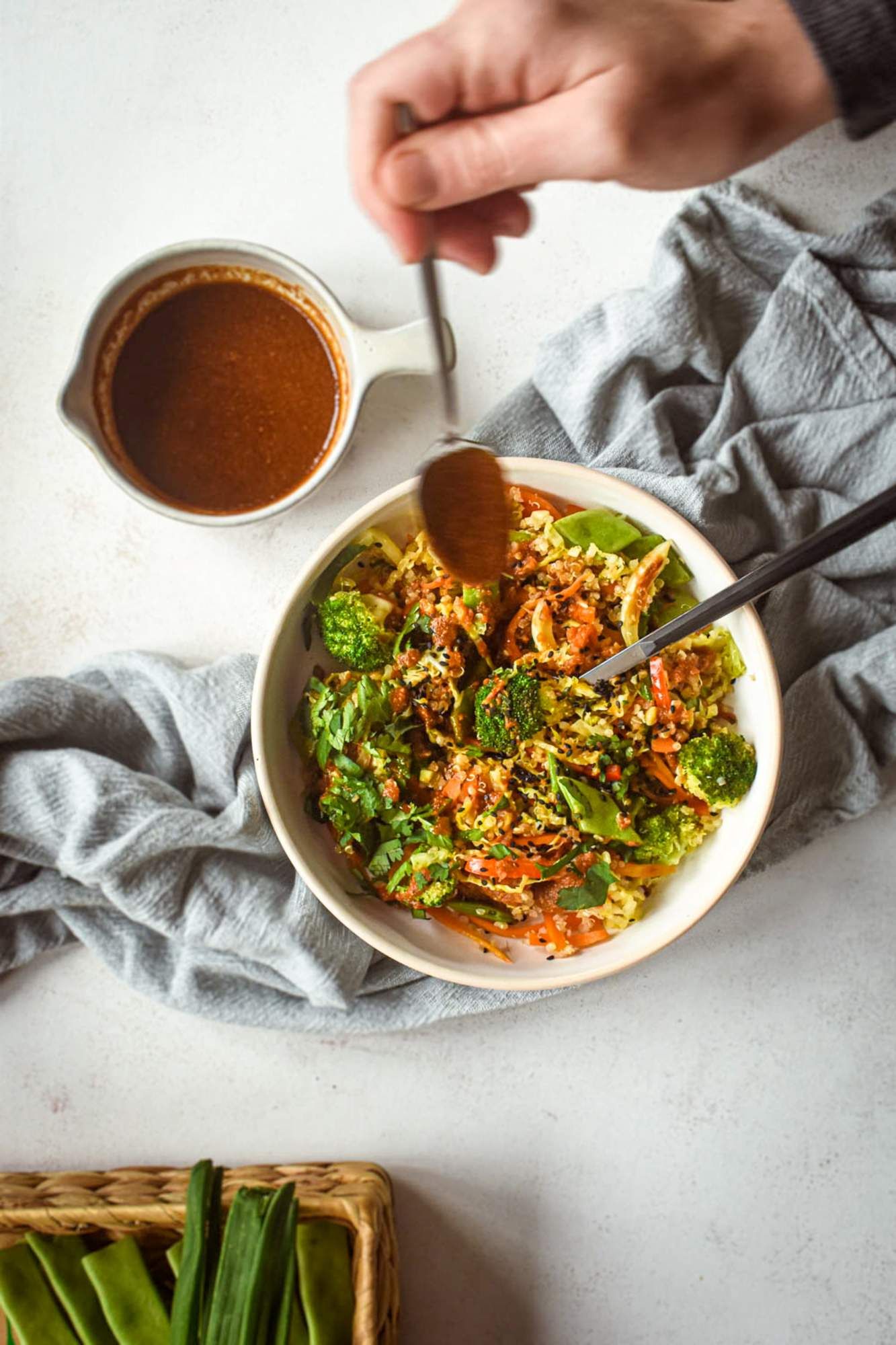 Quinoa and vegetable stir fry in a bowl with a spicy stir fry sauce being drizzled on top with a spoon.