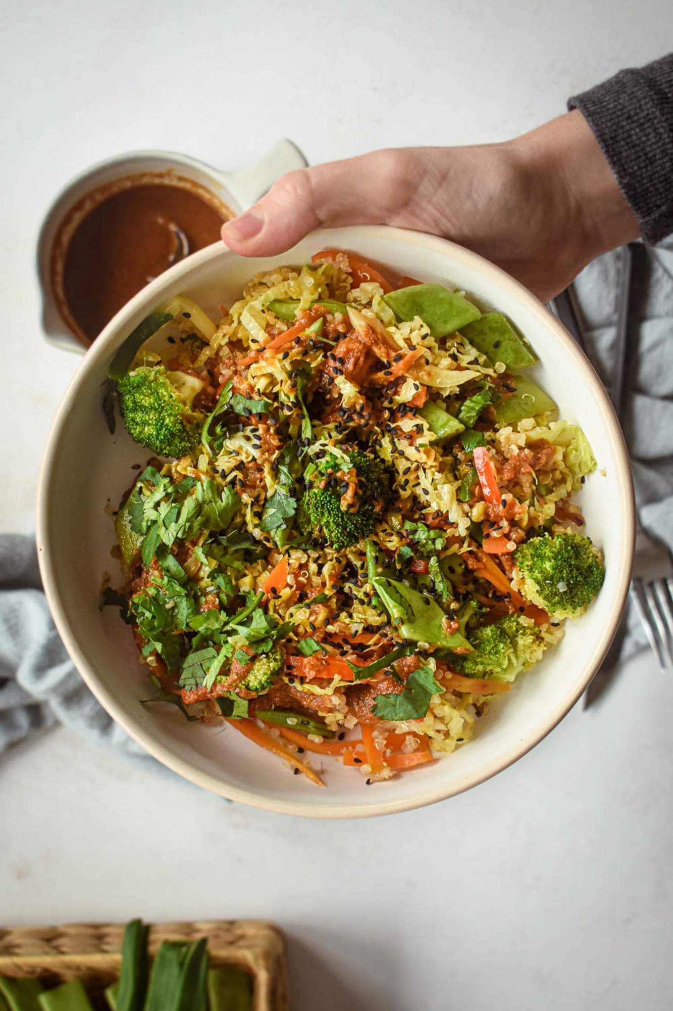 Quinoa stir fry with vegetables in an Asian stir fry sauce in a bowl being held by a hand.