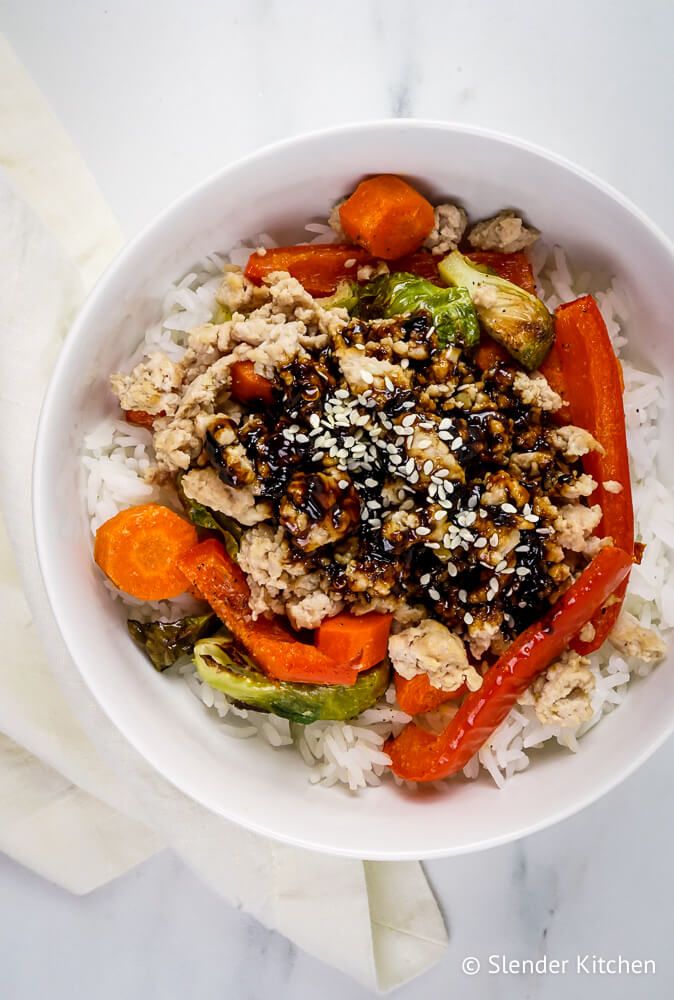 Rice bowls with Asian ingredients including roasted vegetables, ground turkey, and stir fry sauce in a bowl.