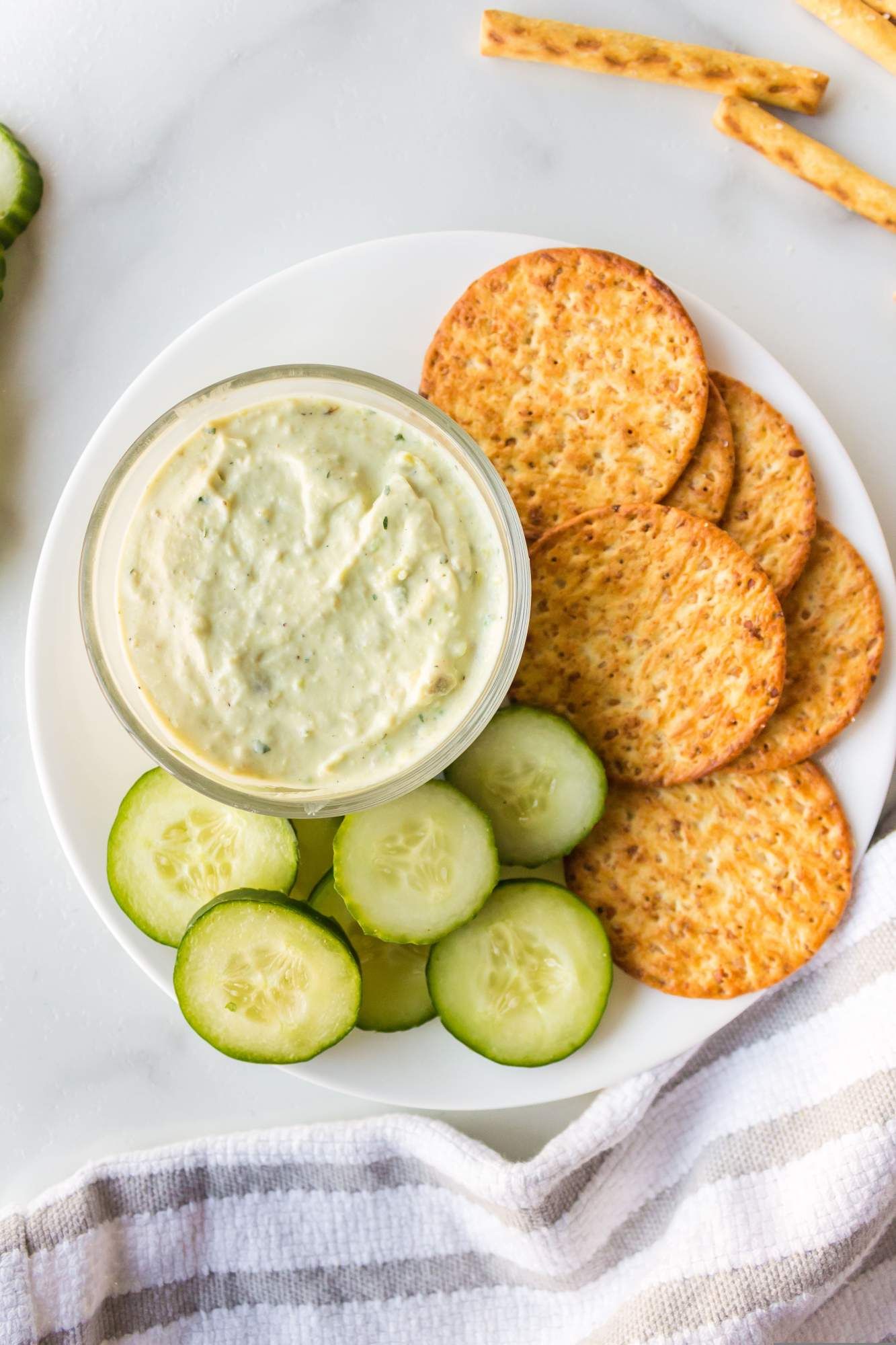 Ranch avocado dip with Greek yogurt on a plate with cucumbers and whole wheat crackers. 