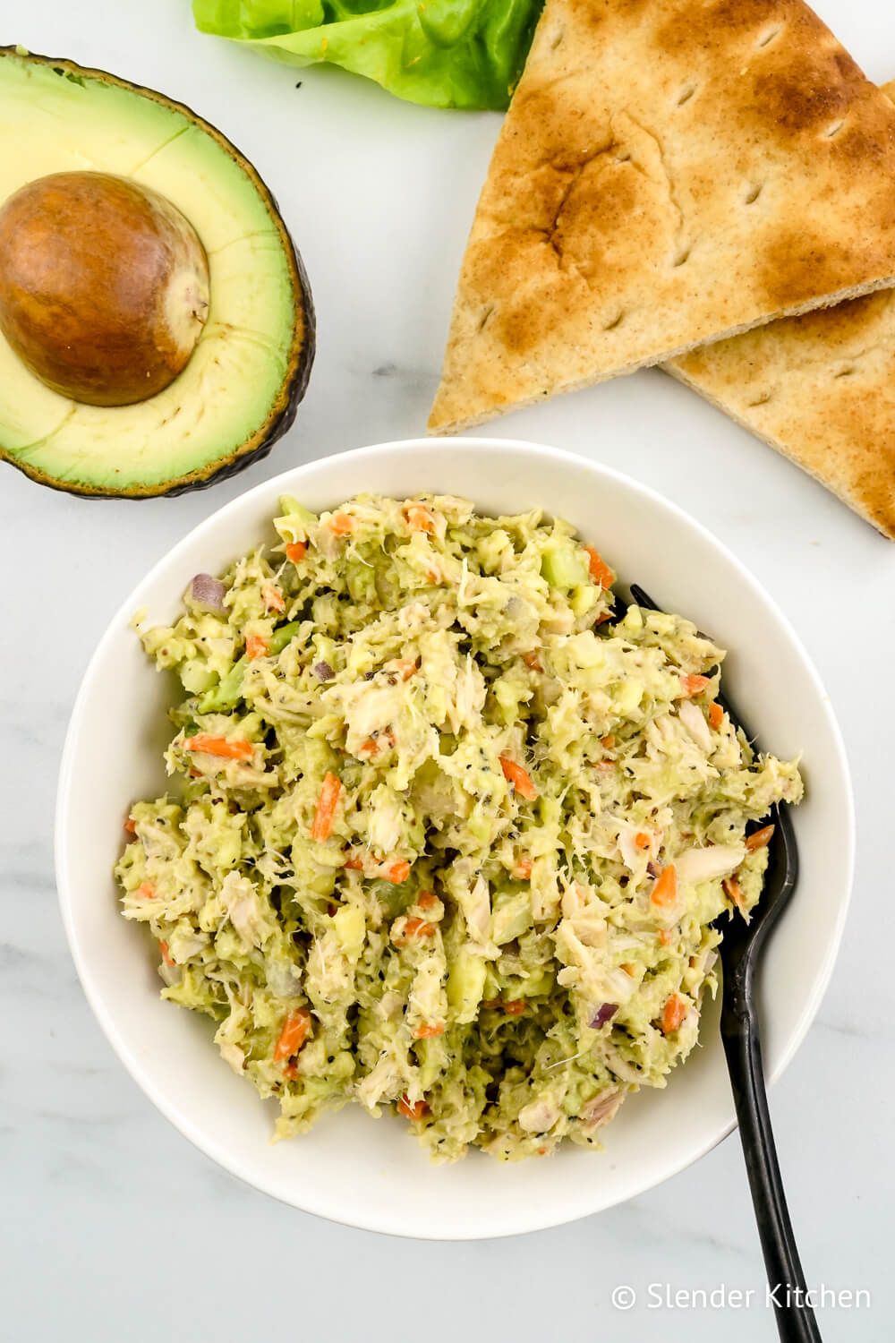 Tuna avocado salad in a bowl with an avocado and lettuce on the side.