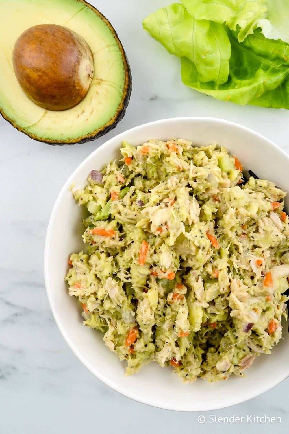 Avocado and tuna salad with carrot and celery in a bowl with avocado on the side.