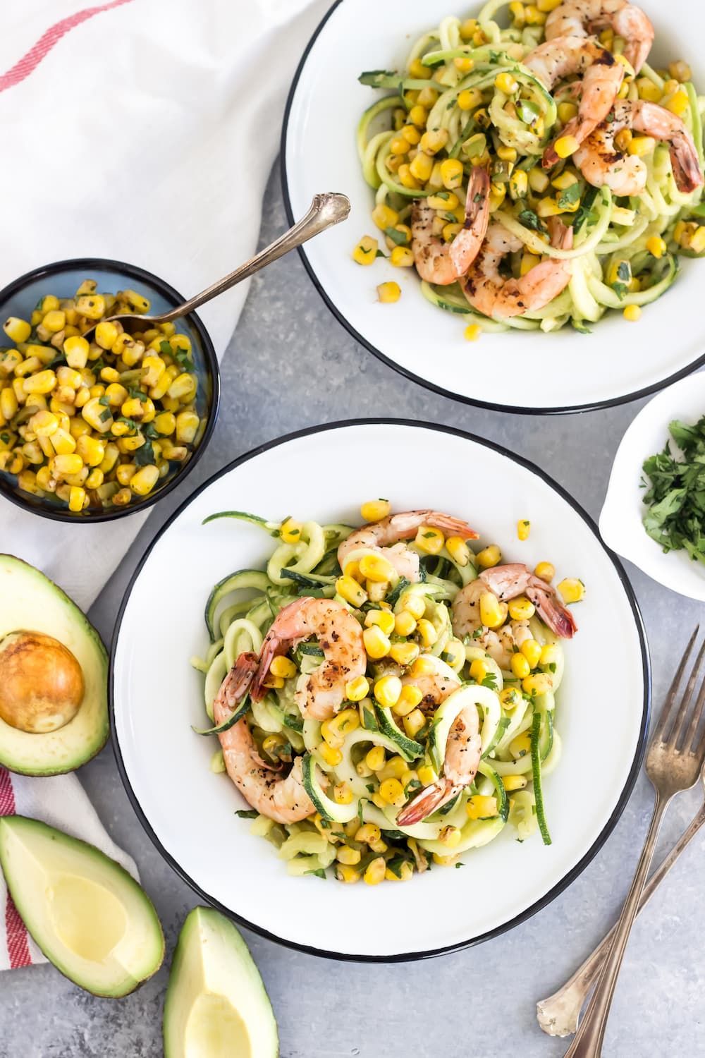 Avocado pasta with shrimp, corn, and zucchini noodles on two plates with corn salsa.