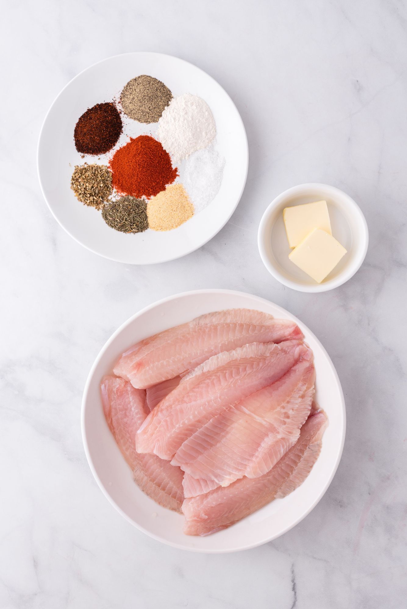 Ingredients for blackened tilapia including spices, butter, and tilapia filets.