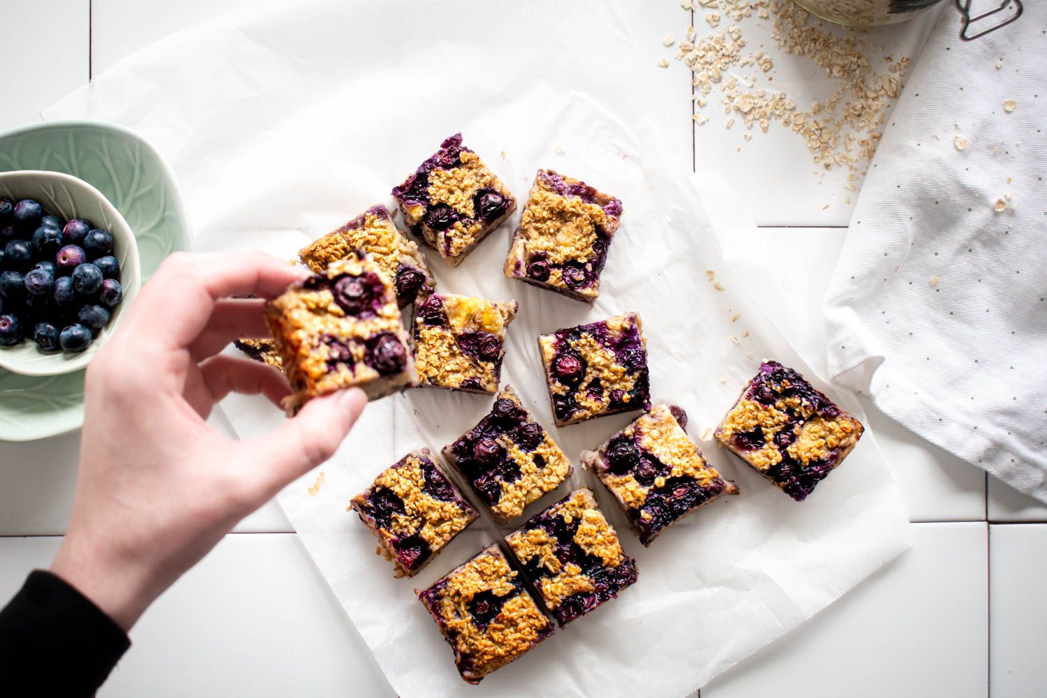 Baked oatmeal with blueberries and banana cut into squares and being picked up by a hand.