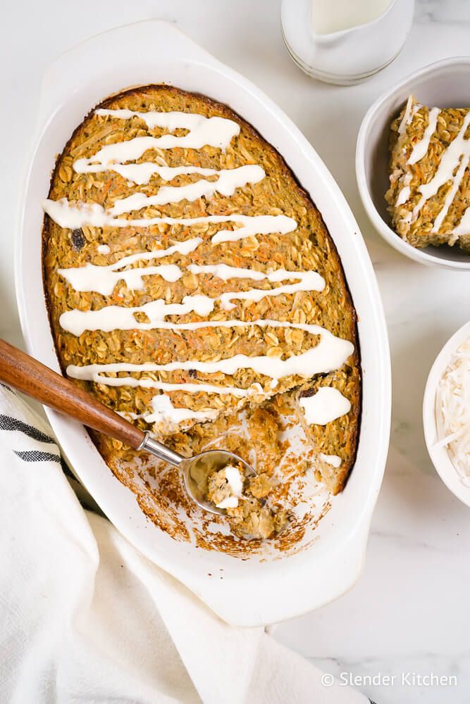 Baked carrot oatmeal with a cream cheese glaze in a baking dish with loose oats on the side.