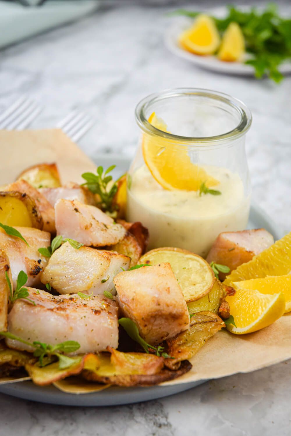 Baked fish and potato chips on a plate with fresh lemon and homemade tartar sauce.