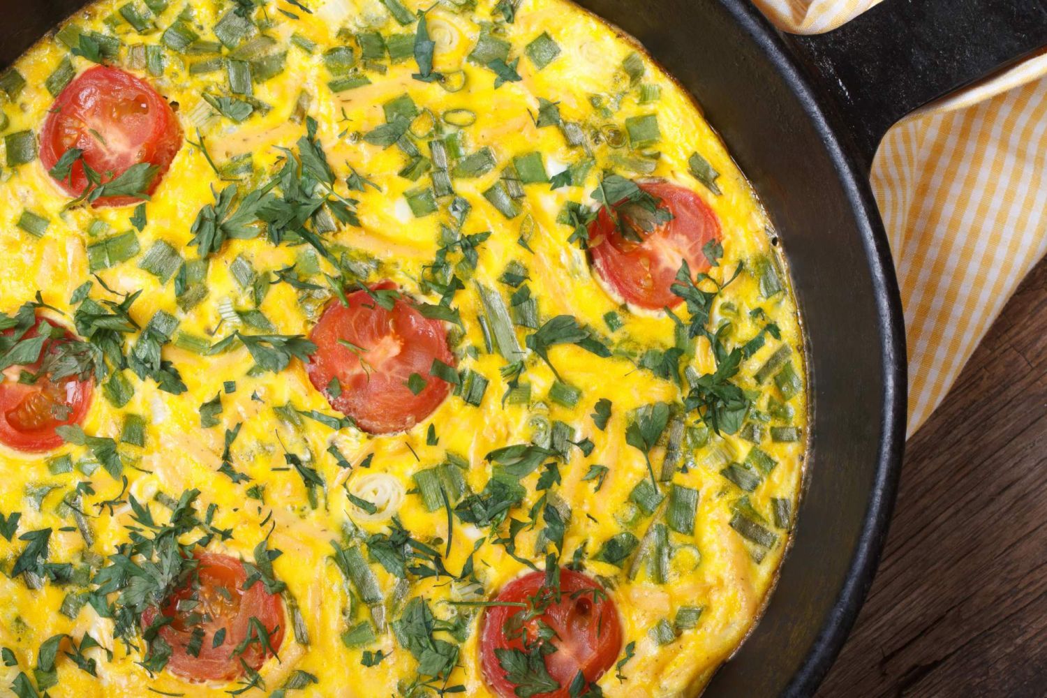 Tomato frittata with goat cheese and herbs in a skillet with a napkin on the side.