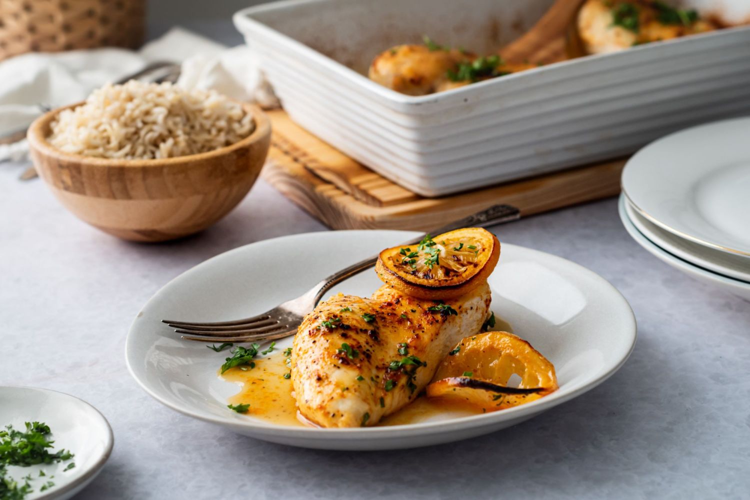 Chicken breasts baked with lemon pepper and lemon slices served on a plate with fresh parsley.