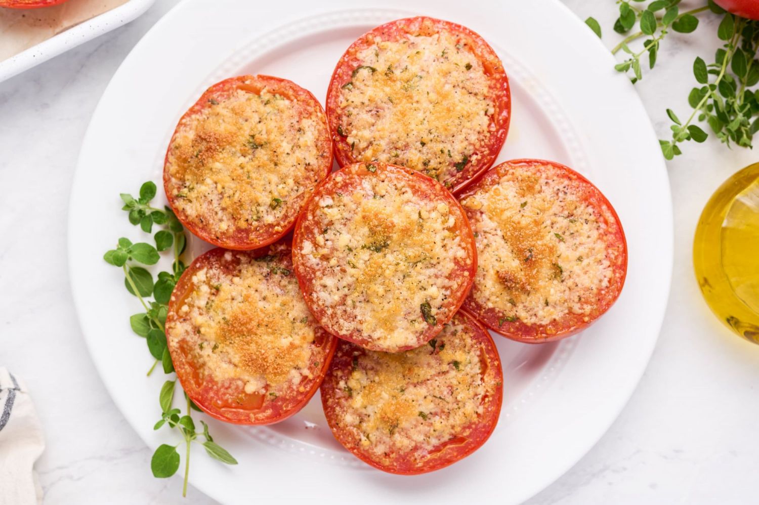 Roasted Parmesan tomatoes on a plate with melted parmesan cheese and fresh herbs.