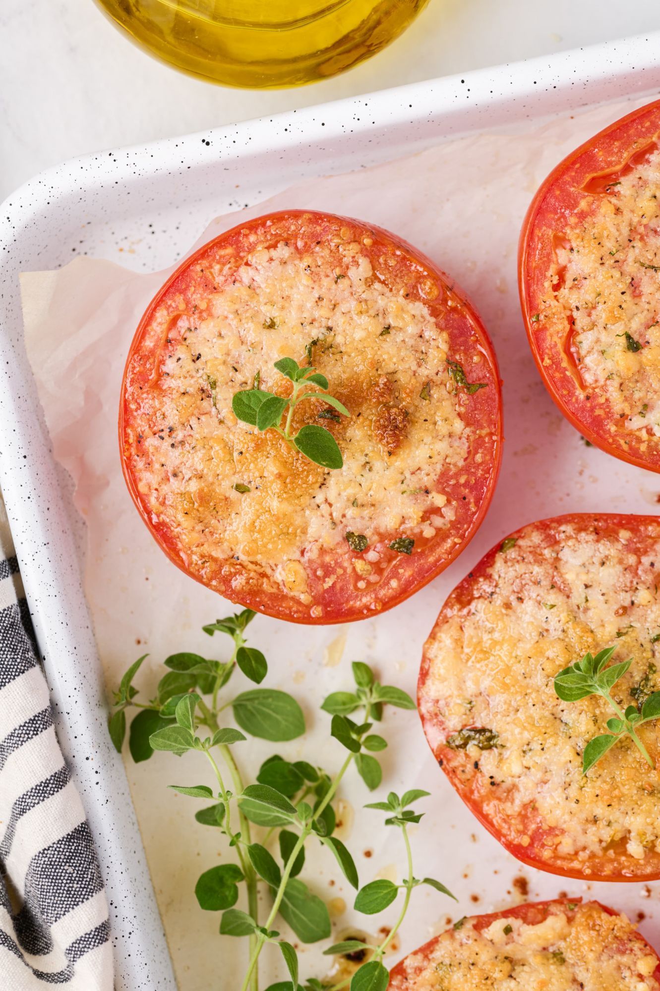 Crispy Parmesan baked tomatoes on a sheet pan with fresh oregano.