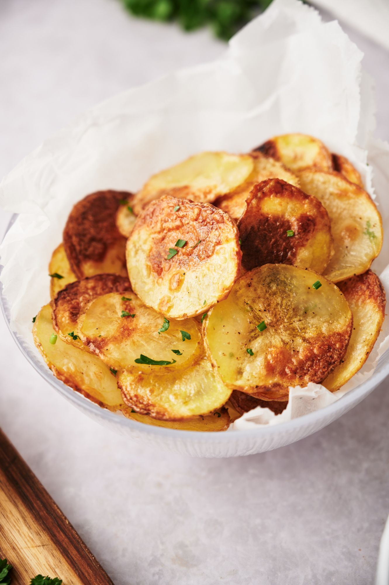 Crispy baked potato chips in a bowl with browned edges and parsley.