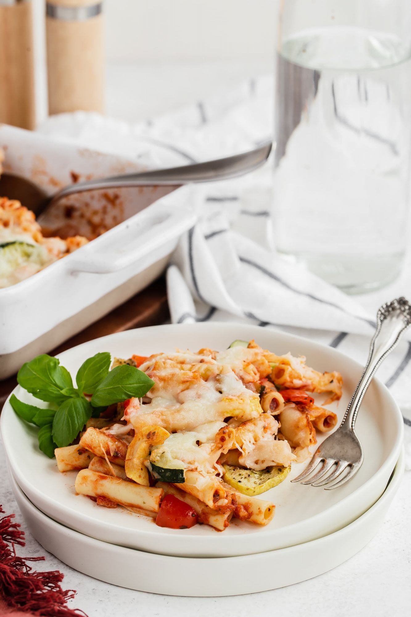 Roasted vegetables baked ziti served on a plate with zucchini, summer squash, melted cheese, and fresh basil.