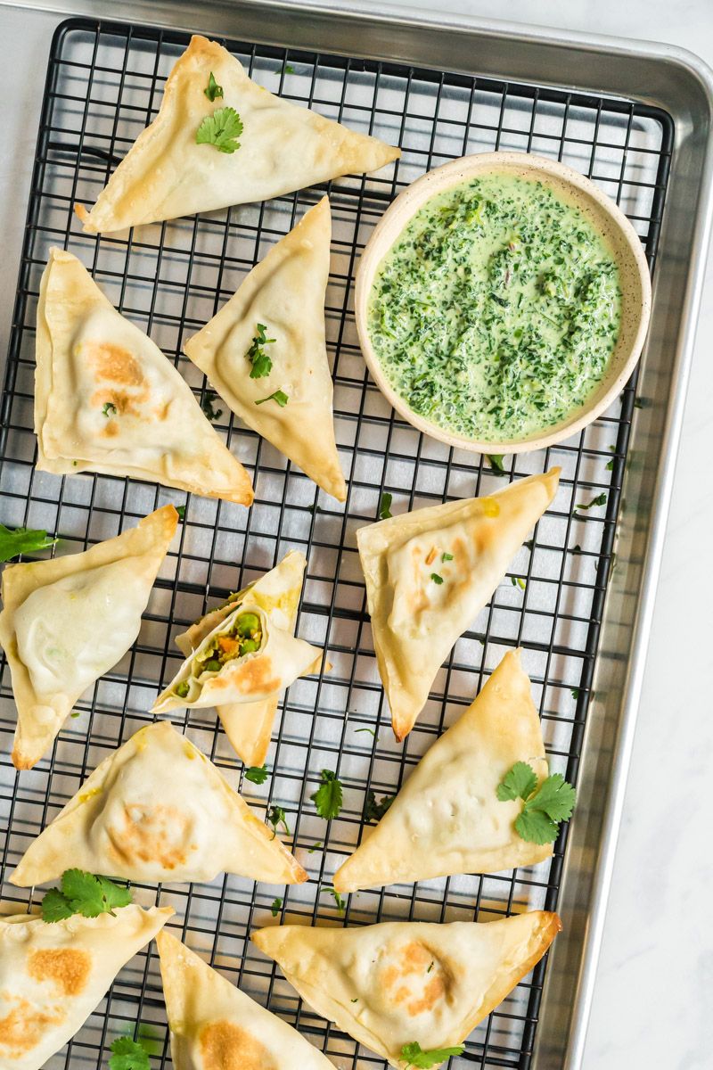 Samosa made with wonton wrappers and filled with potatoes, carrots, peas, and cauliflower on a wire rack with cilantro.