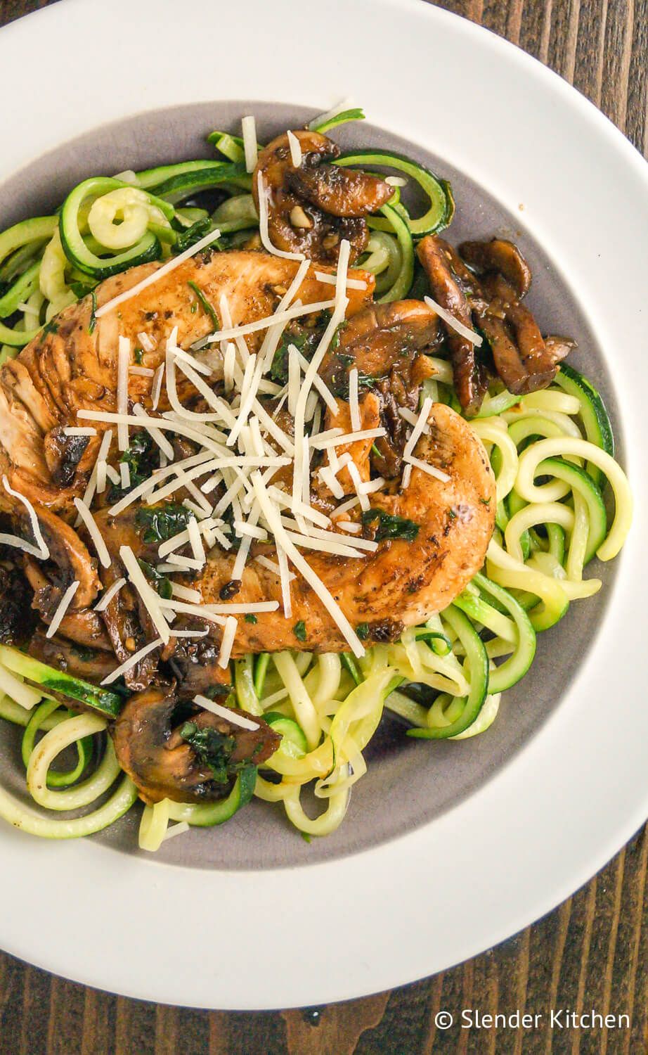 Balsamic chicken with zucchini noodles on a white plate and wood background.