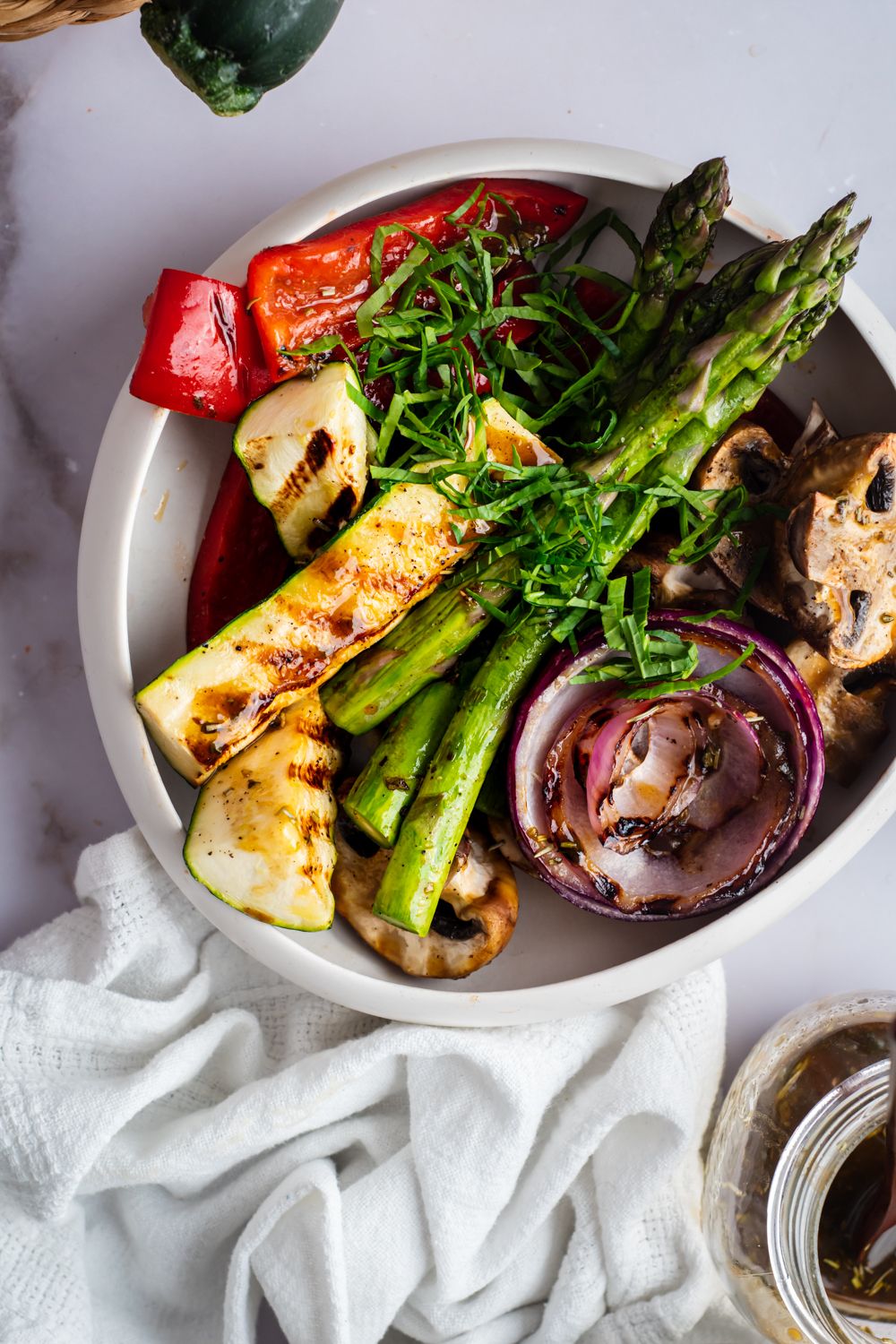 Balsamic marinade for grilled vegetables drizzled on a bowl of asparagus, zucchini, bell peppers, onions, and mushrooms.